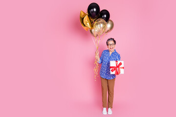 Full size photo of funky person dressed print blouse pants holding balloons gift near empty space isolated on pink color background