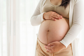 An Asian young pregnant wife relaxes at home, her hand gently resting on her belly, filled with love and anticipation as she embraces the journey of impending motherhood.