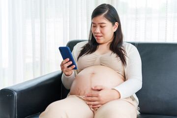 An Asian young pregnant wife relaxes on the sofa at home, filled with love and anticipation, preparing for the arrival of her baby while embracing the journey of motherhood.