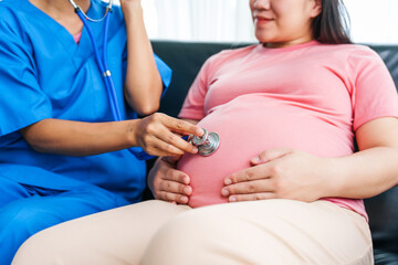 Asian female doctor and nurse perform an ultrasound on a pregnant woman, using a stethoscope and...