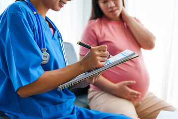 Asian female doctor and nurse consult on sofa with a pregnant woman, using ultrasound and...