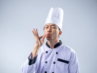 A satisfied Asian male chef in a white chef's uniform and hat, making an 