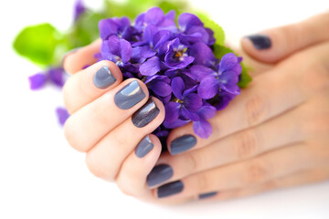 Hands of a woman with dark manicure on nails and bouquet of violets on a white background