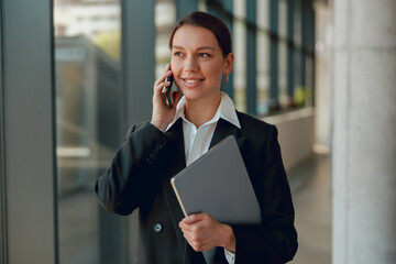 Businesswoman talking on the phone while holding a folder in a modern office building