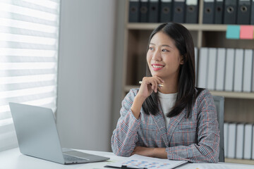 Sharing good business news. Attractive young businesswoman talking on the mobile phone and smiling while sitting at her working place in office and looking at laptop PC.