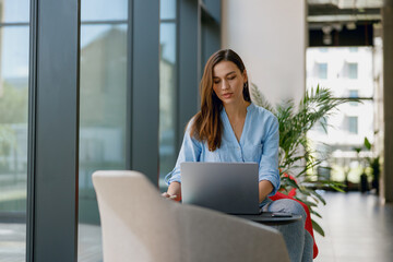 A woman is seen inside a contemporary green office, concentrating on work using a laptop