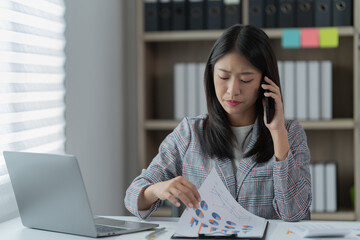 Sharing good business news. Attractive young businesswoman talking on the mobile phone and smiling while sitting at her working place in office and looking at laptop PC.