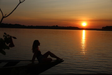 mulher sentada em canoa no p&ocirc;r do sol no lago acajutuba, em Iranduba, Amazonas 