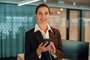 A professional businesswoman is seen utilizing a smartphone in a contemporary office setting