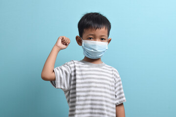 Asian Boy wearing health mask isolated on blue background. Confident kid shows his biceps arm muscle. Medical and health concept