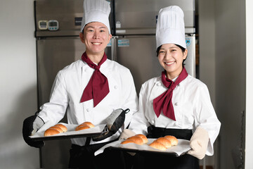 厨房でパンを製造する笑顔のアジア人男女