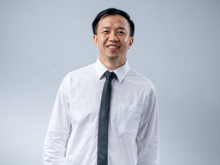 Asian businessman in a white shirt and black tie smiling confidently, standing sideways against a plain light background. The image portrays confidence, professionalism, and success
