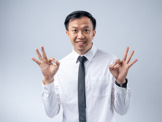 Asian businessman in a white shirt and black tie making an OK gesture with his hand, smiling...