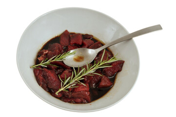 Saladier de viande de bœuf marinée avec du romarin et une cuillère en gros plan sur fond blanc