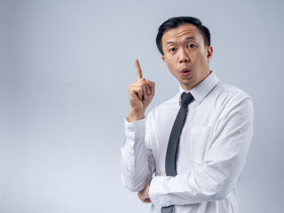 Asian businessman in a white shirt and black tie raising his index finger as if sharing an idea, looking up with an excited expression against a plain light background. The image conveys innovation