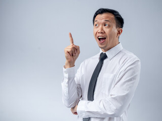 Asian businessman in a white shirt and black tie raising his index finger as if sharing an idea, looking up with an excited expression against a plain light background. The image conveys innovation