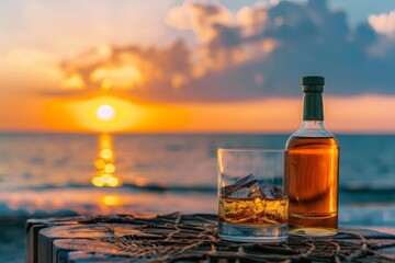 Obraz premium Bottle and glass of Whisky on a table with beach sea and sunset in background