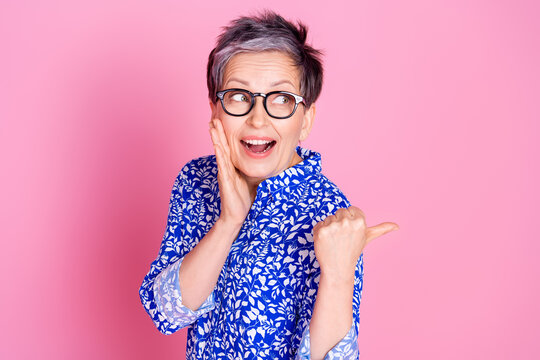 Photo of astonished person with gray hair dressed blouse in glasses directing look at sale empty space isolated on pink color background