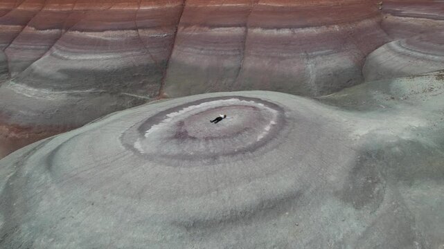 Aerial View of Lonely Woman Lying on Top of Swirled Sandstone Hill in Landscape Reminiscent of Mars, Drone Shot