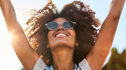 Joyful young woman with arms raised, celebrating happiness and freedom in the bright sunlight.