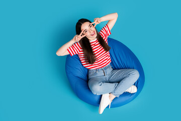 Full length top view photo of shiny attractive lady dressed red t-shirt bean bag showing v-signs empty space isolated blue color background