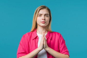 Young woman praying, begs to apologize, guilty. Blue studio. Hopeful prayer.