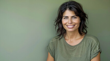 Fototapeta premium Playful and relaxed woman with tousled dark hair and an engaging smile in a green shirt, against a soft green background