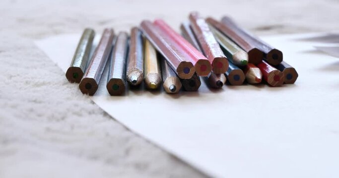 A set of multicolored pencils that lie on a piece of paper. On soft carpet there is a pack of pencils of different colors. The video ends when a white piece of paper enters frame and covers lens. 