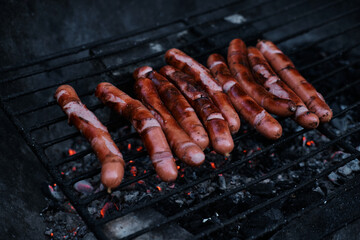 BBQ with fiery sausages on the grill. Grilling food, bbq, barbecue. German sausages are cooked on hot coals in the grill. Close up view, soft blurred background.