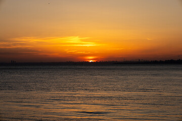 Fototapeta premium Stunning Sunset Over the Calm Waters with a City Skyline in the Distance