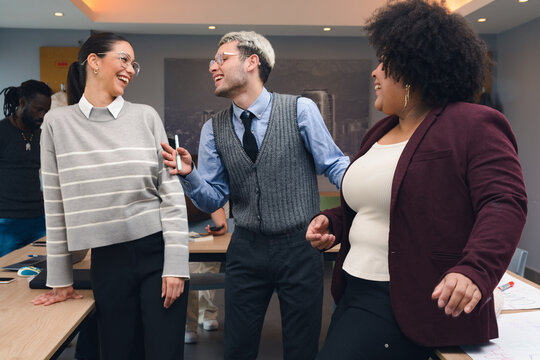 Three People are standing around a table, smiling and laughing during the work meeting