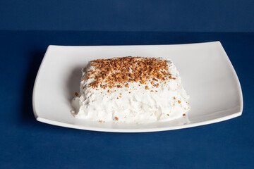 Exquisite dessert presentation featuring a mound of whipped cheese topped with a sprinkle of crumbled almond topping on a white rectangular plate against a dark blue background with copy space.