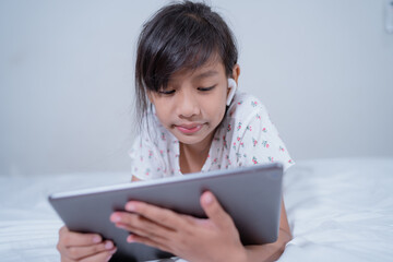 smiling Little girl with headphones and tablet computer listening to music at home.Cute girl communicates online with friends via internet headphones with microphone.