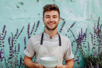 Smiling Young Chef Holding Bowls Against Rustic Blue Wall Background with Lavender Flowers