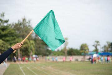 Hand holding a green flag as start or go sign at a sports field.