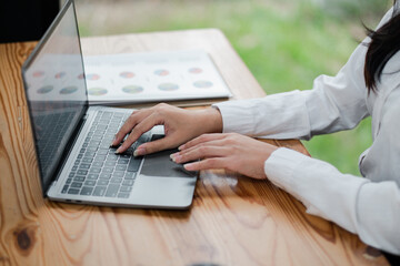 Close-up of hands typing on a laptop at a wooden desk with charts in the background, representing a modern office environment and productive workday.