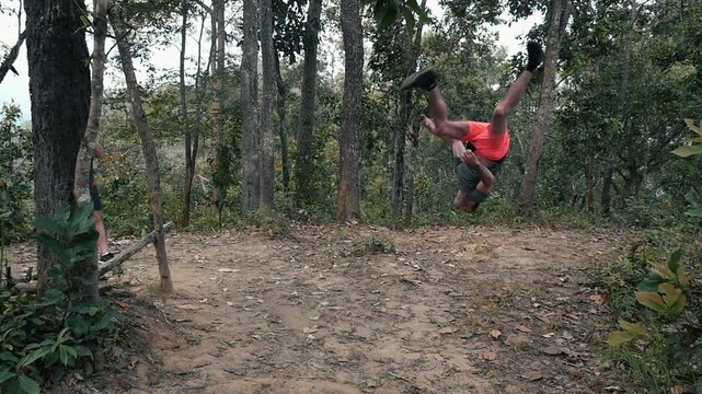 A man does a backlip in slow motion in the forest