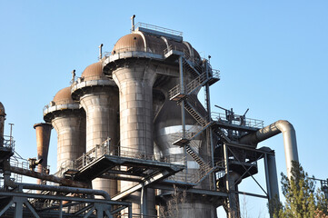 The photograph depicts an old metallurgical plant in Duisburg. Rusty metal structures and pipes dominate the foreground, highlighting the industrial heritage of heavy steel production. The factory's c