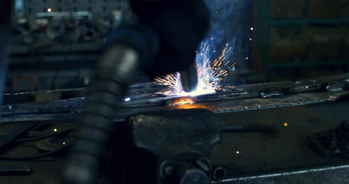 Super slow motion close up of welder blacksmith is welding metal steel with industrial tool with flying sparks in workshop at 1000 fps.