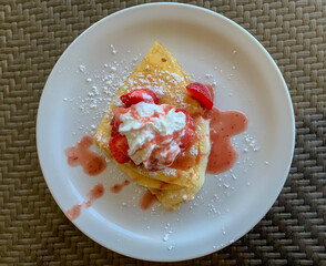 Top view of cream stuffed crepes topped with whipped cream, strawberries and strawberry sauce.