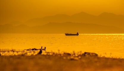 A fisherman on boat at sunset and mountains hills in background, golden hour, patratu, ranchi, jharkhand, india