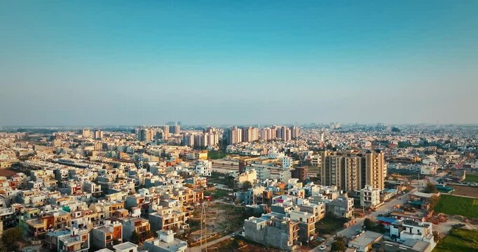 Drone flies left and up, then pans right, revealing Mohali, Punjab&rsquo;s dense urban settlement and rising skyscrapers in crisp winter air and warm morning golden light.