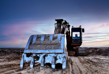 Excavator on groundwork on dramatic twilight. Excavator on sunset background. Open-pit mining. Backhoe dig ground in quarry. Heavy construction equipment on excavation on construction site.