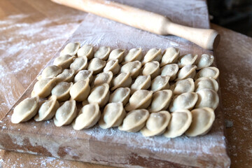 Raw dumplings were laid out on a wooden board for cooking. Next to it is a rolling pin for rolling out the dough. The filling is minced meat, potatoes, cheese or cottage cheese.