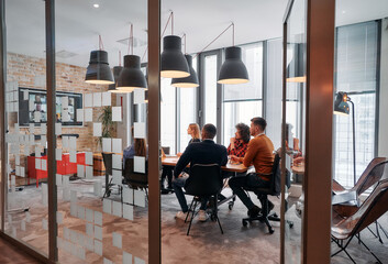 In a sleek glass office space, a team of business professionals engage in lively discussions and exchange strategic ideas, showcasing collaboration and innovation at the heart of modern corporate