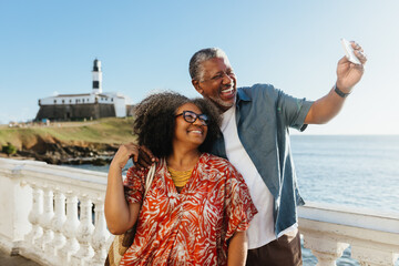 Morden Retirement: Elderly couple taking a selfie at the seaside with a lighthouse in the background