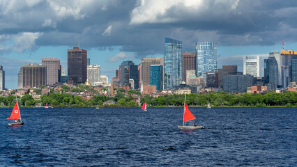 Red sailboats gliding on the Charles River's calm waters with the skyline of Boston, Massachusetts, USA