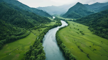Aerial view of a winding river meandering through a lush green valley surrounded by forested hills, creating a peaceful natural landscape.
