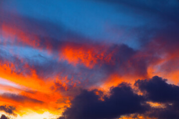 Fototapeta premium Sky is filled with clouds and the sun is setting. The clouds are orange and pink, creating a beautiful and serene atmosphere