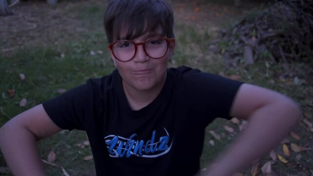 Close up , low angle shot of caucasian 10 years old boy with glasses, talking and taunting to camera, garden leaves in the background